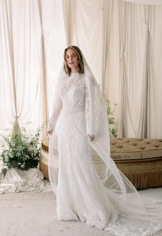 Woman in a white wedding dress with a long veil standing in a decorated room.