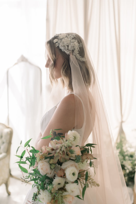 Bride holding a bouquet with a lace veil and floral headpiece indoors.