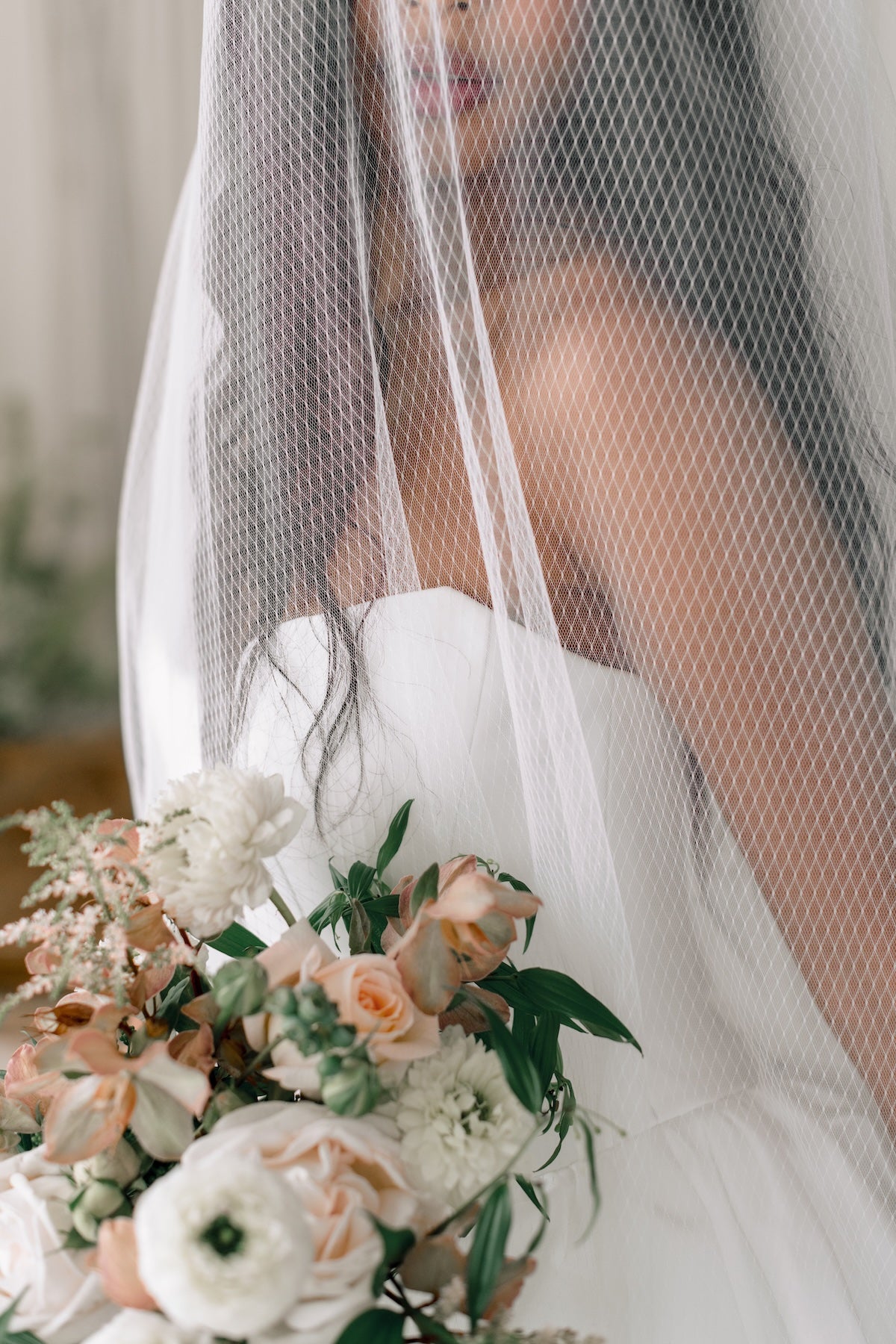 Bride holding a bouquet of flowers with a veil in the background