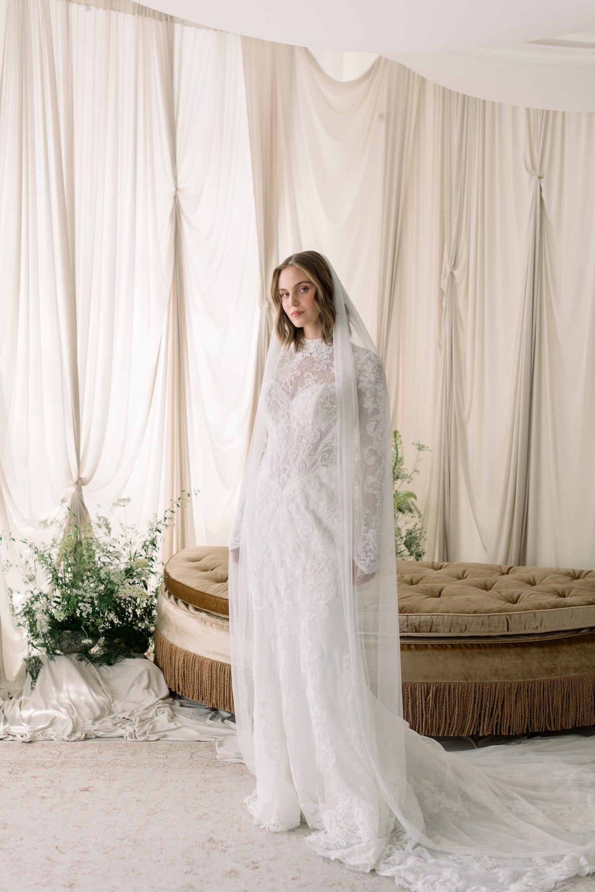 Woman in a white wedding dress with a long veil standing in a decorated room.