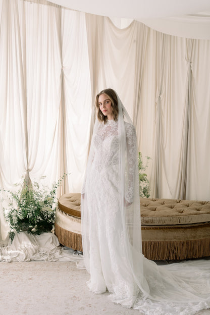 Woman in a white wedding dress with a long veil standing in a decorated room.