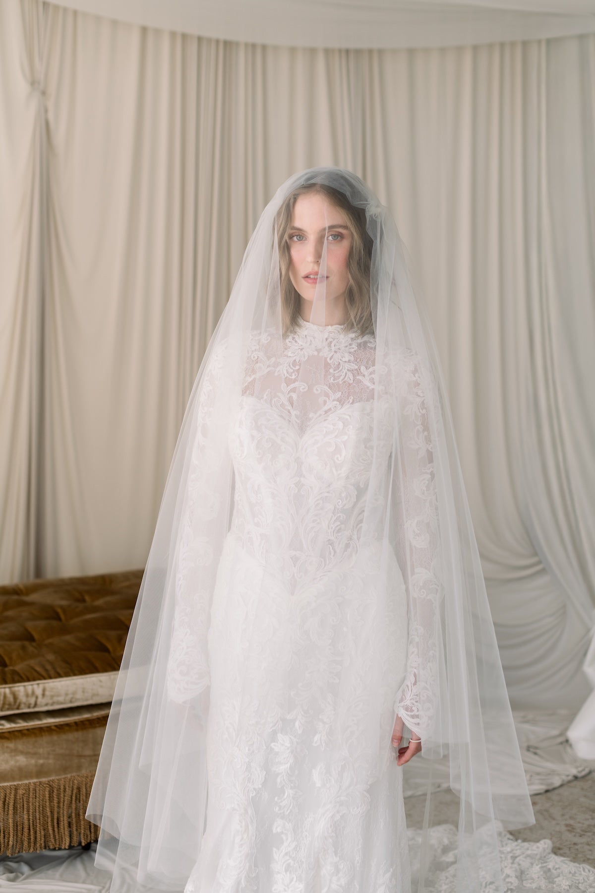 Woman wearing a white wedding dress with a long veil in a softly lit room.