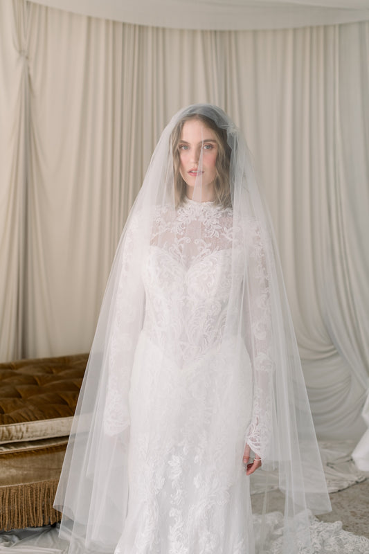 Woman wearing a white wedding dress with a long veil in a softly lit room.