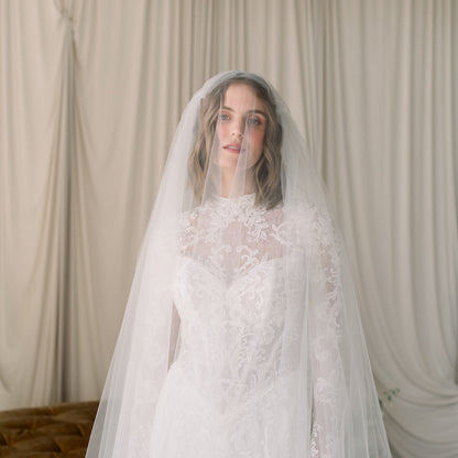 Woman wearing a white lace wedding dress with a matching veil against a neutral background