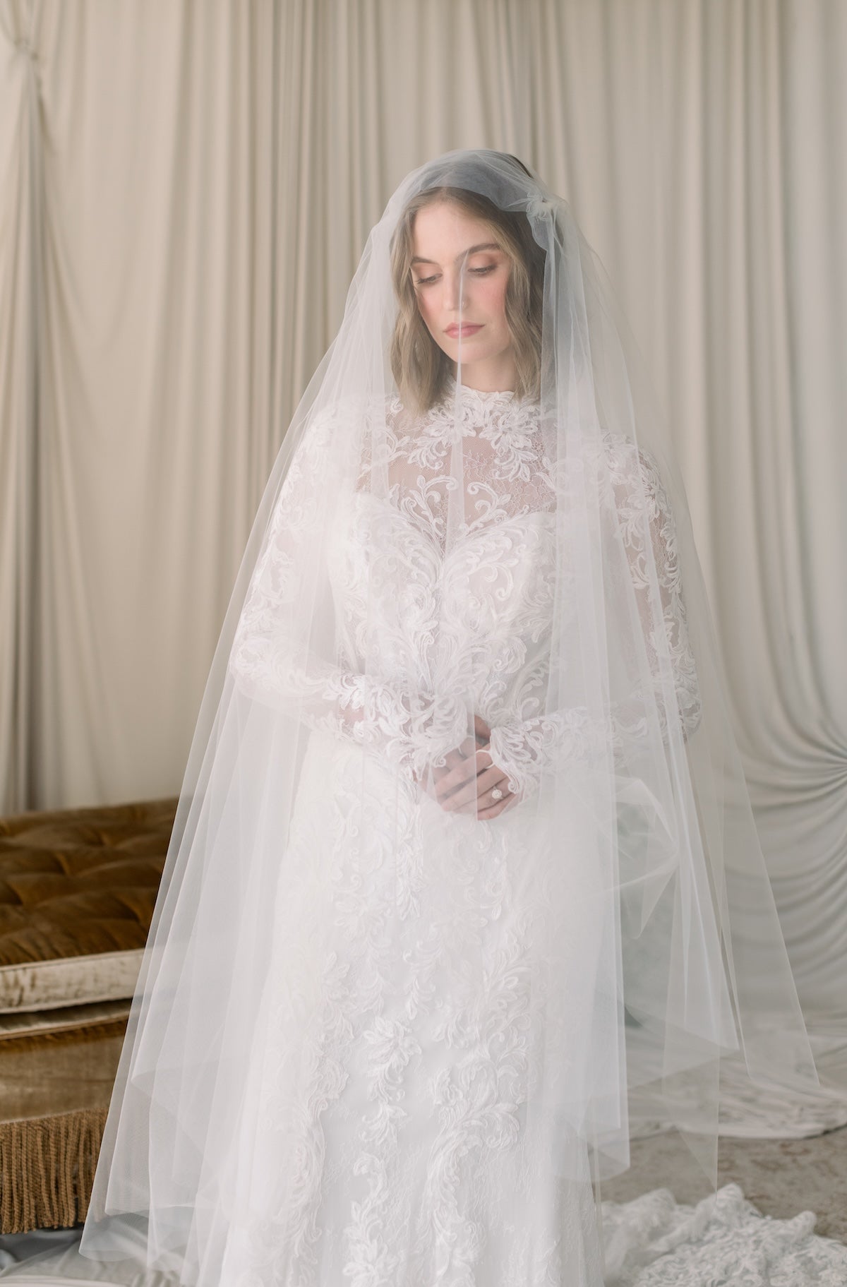 Woman wearing a white lace wedding dress with a veil against a neutral background
