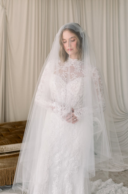 Woman wearing a white lace wedding dress with a veil against a neutral background