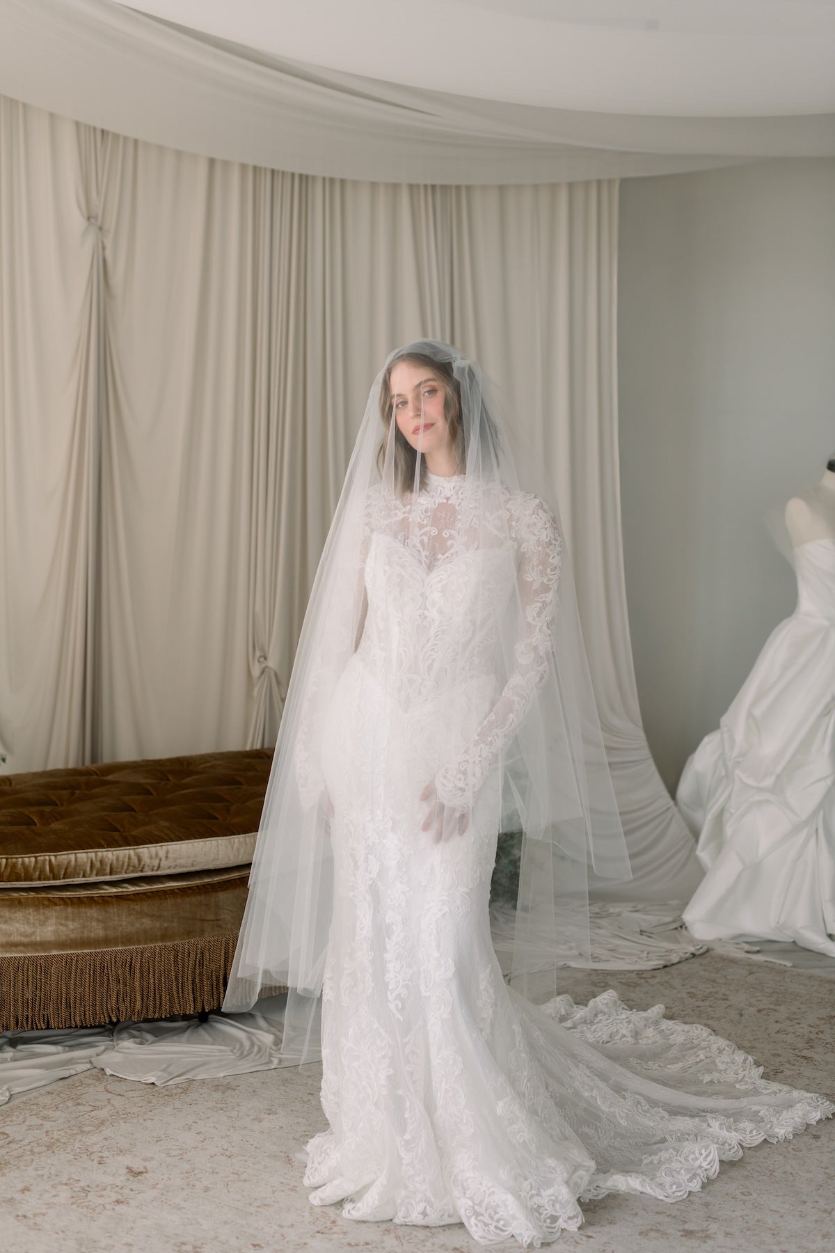 Woman wearing a white lace wedding dress with a long train in a room with curtains.