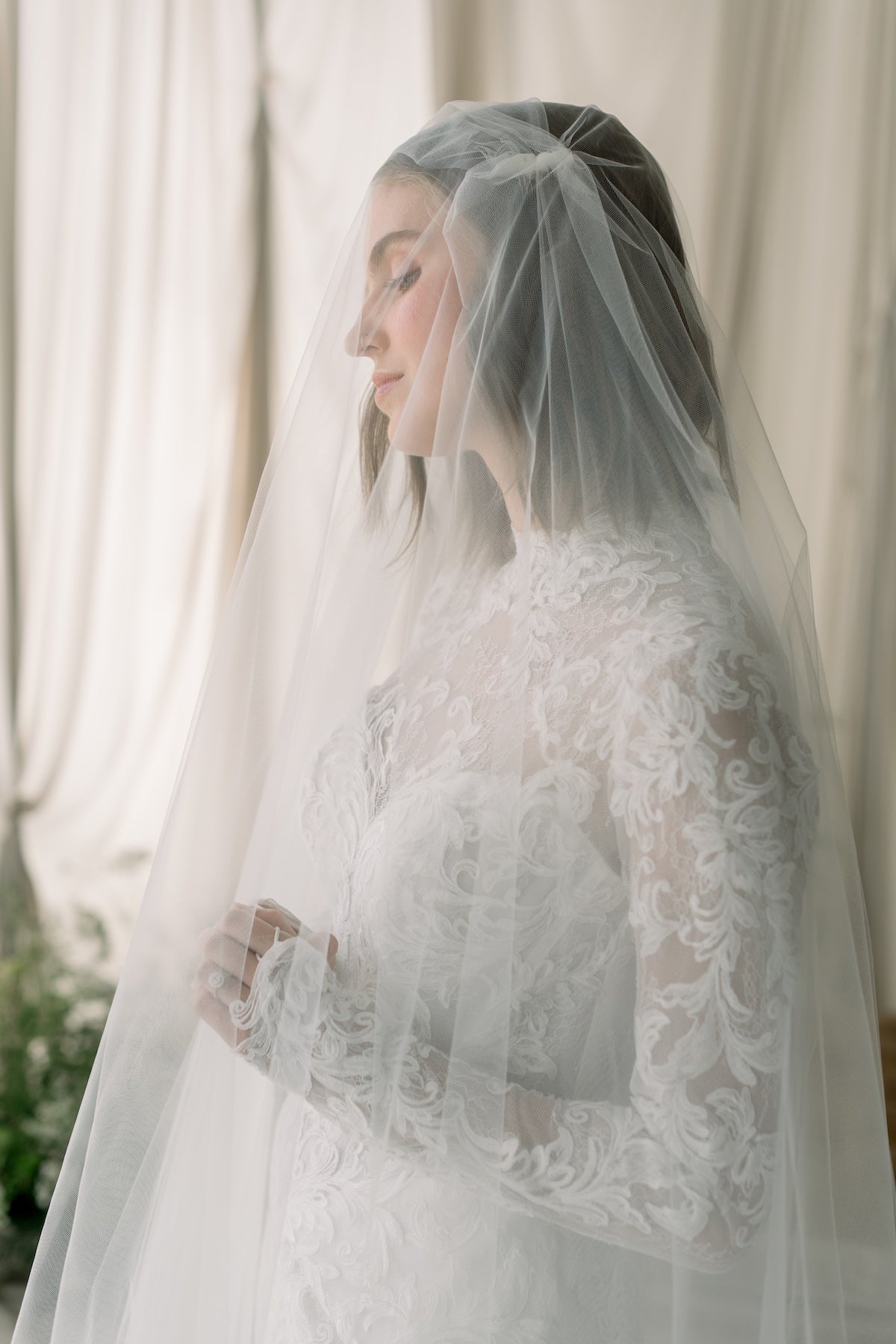 Woman wearing a white lace wedding dress with a veil against a neutral background