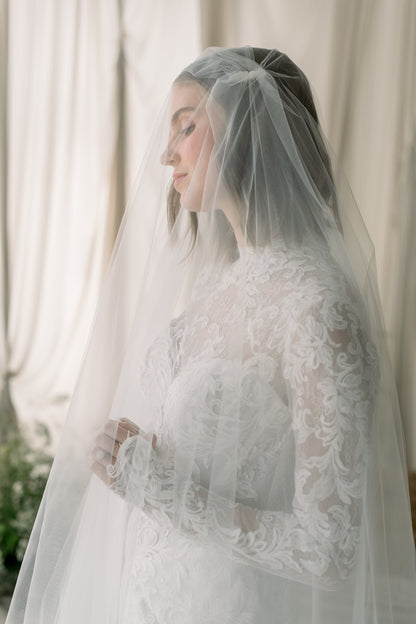 Woman wearing a white lace wedding dress with a veil against a neutral background