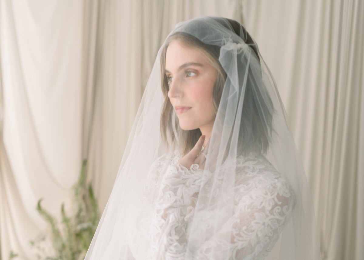 Woman wearing a white wedding dress with a veil in a softly lit room.