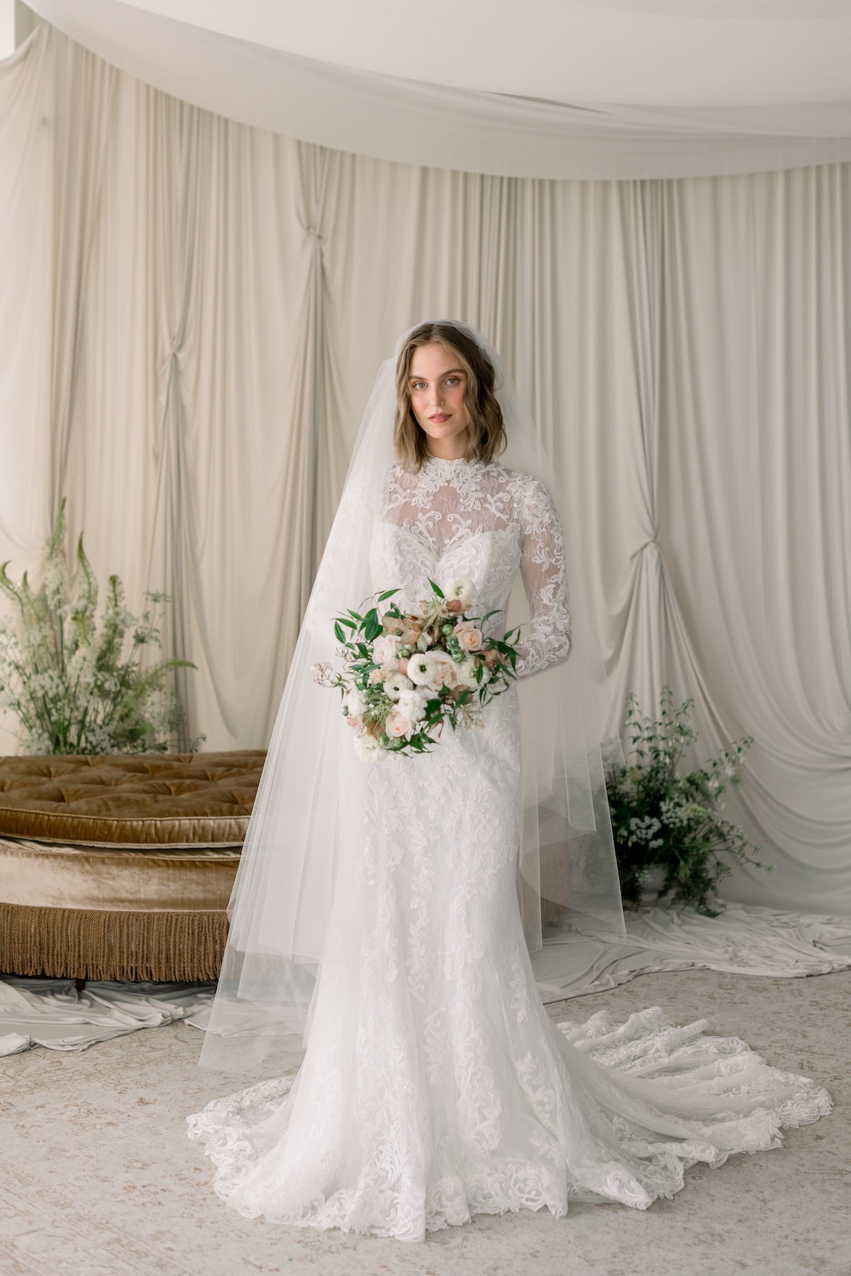 Bride in a lace wedding dress holding a bouquet in a decorated indoor setting.