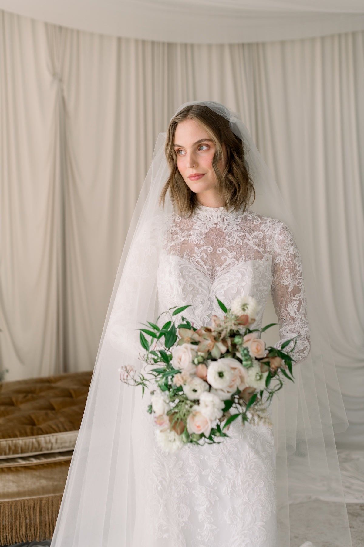 Bride holding a bouquet in a softly lit room with curtains