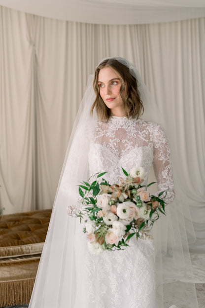 Bride holding a bouquet in a softly lit room with curtains