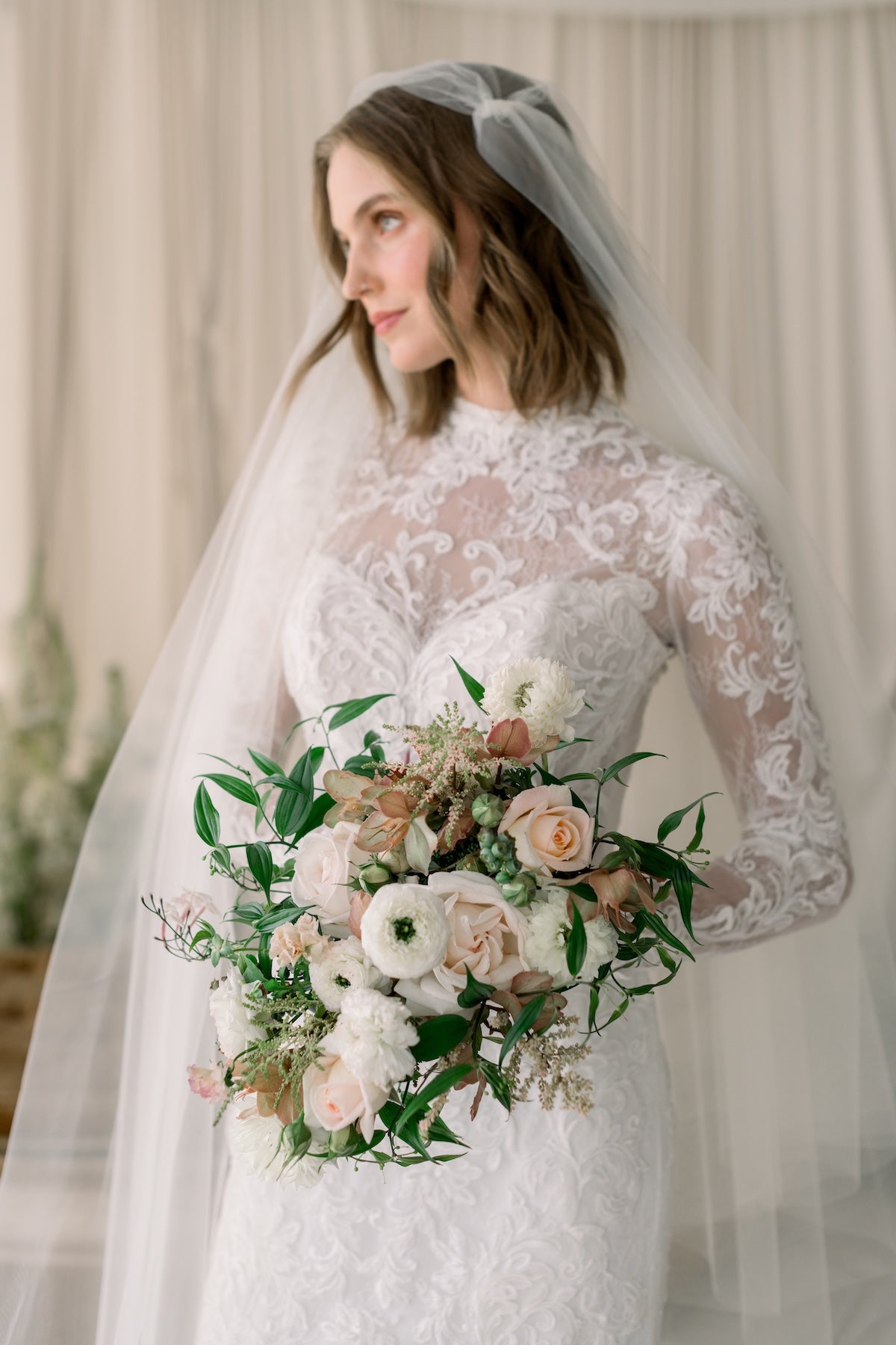 Bride in a lace wedding dress holding a bouquet with a veil and floral background