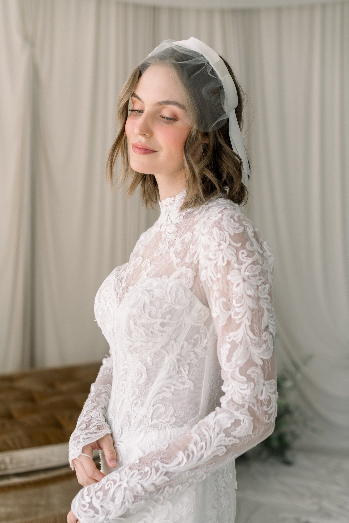 Woman wearing a white lace dress with a veil against a neutral background