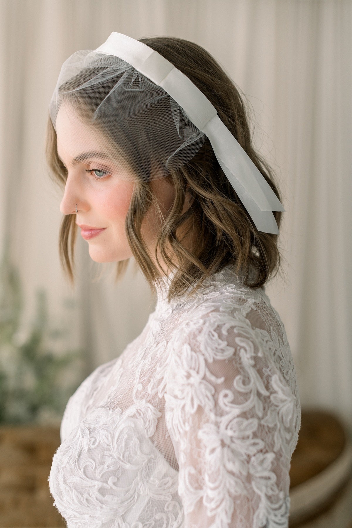 Woman wearing a white lace dress and veil against a neutral background