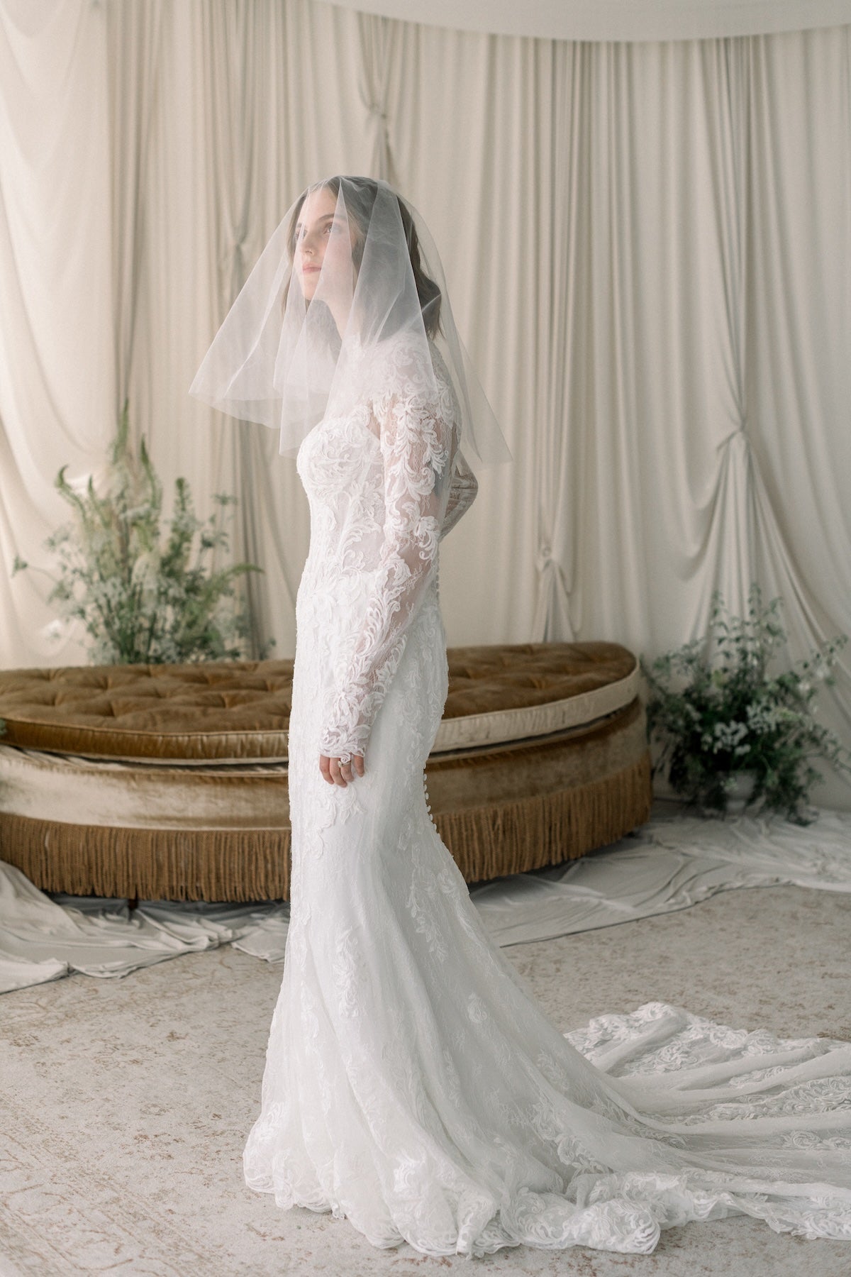 Bride in a white wedding dress with a long veil standing in a decorated room.