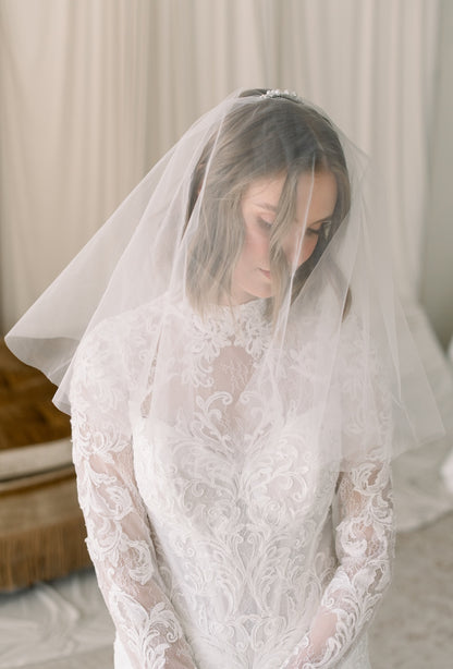 Woman wearing a lace wedding dress with a veil indoors.