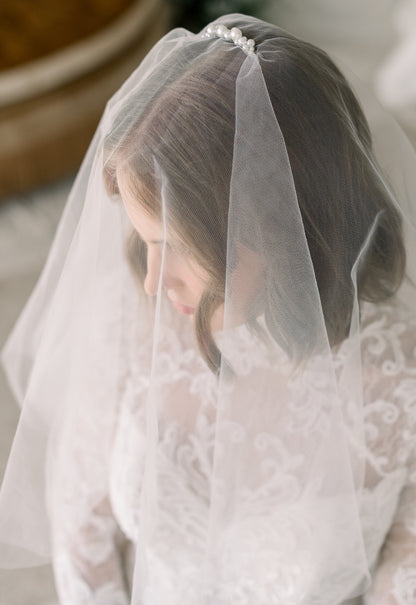 Person wearing a white lace veil and dress, with a blurred background