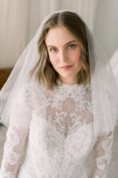 Woman wearing a white lace wedding dress with a veil against a neutral background
