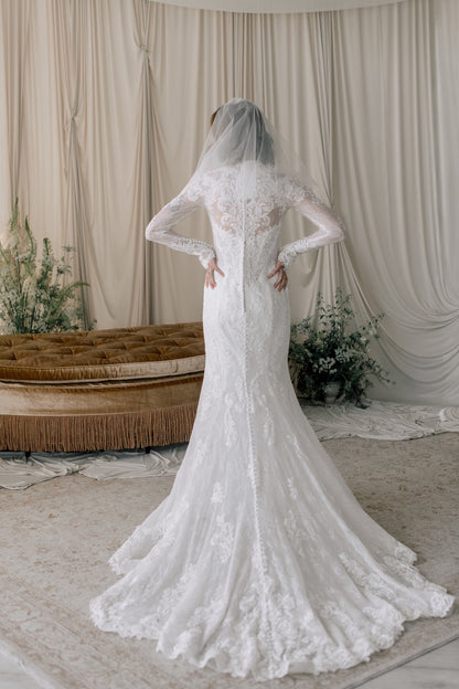 White lace wedding dress with long sleeves in a softly lit room.