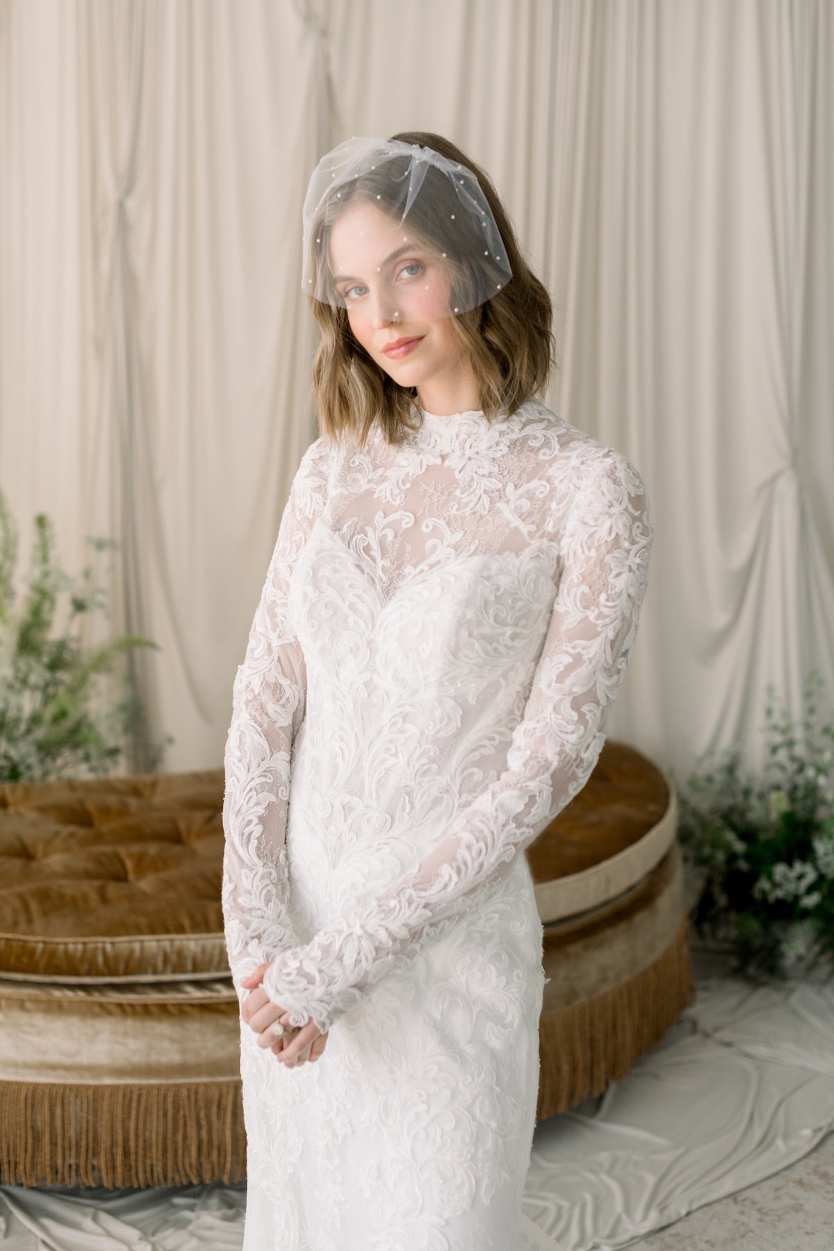 Woman wearing a white lace dress with a sheer veil in a softly lit room.