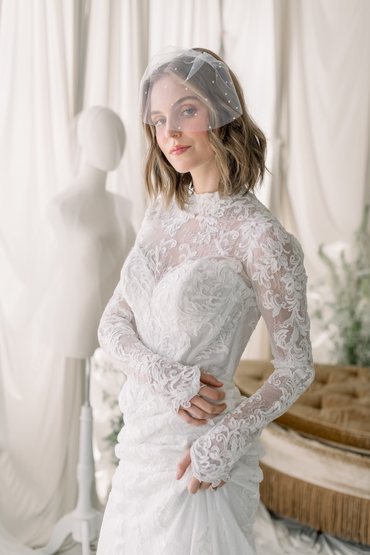 Woman wearing a lace wedding dress with a veil in a softly lit room.