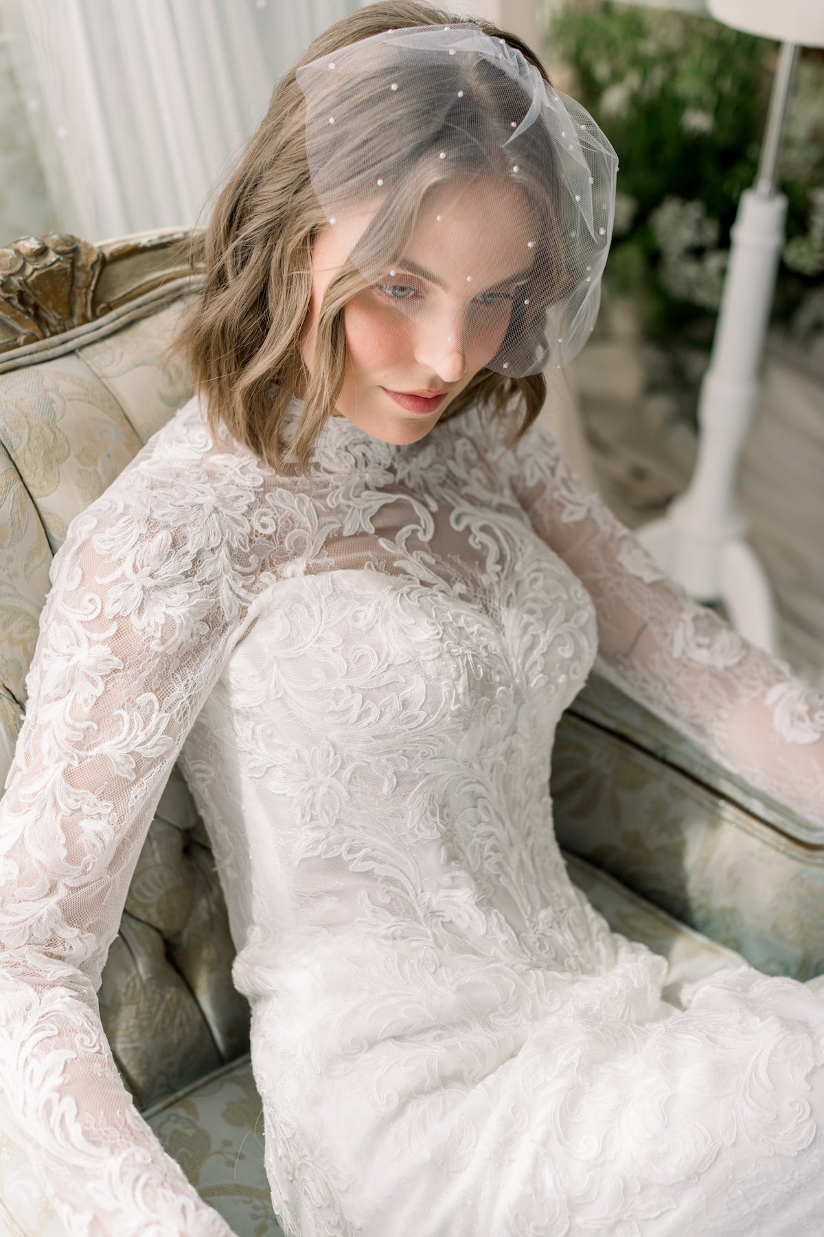 Woman in a white lace wedding dress sitting on a couch with a veil.