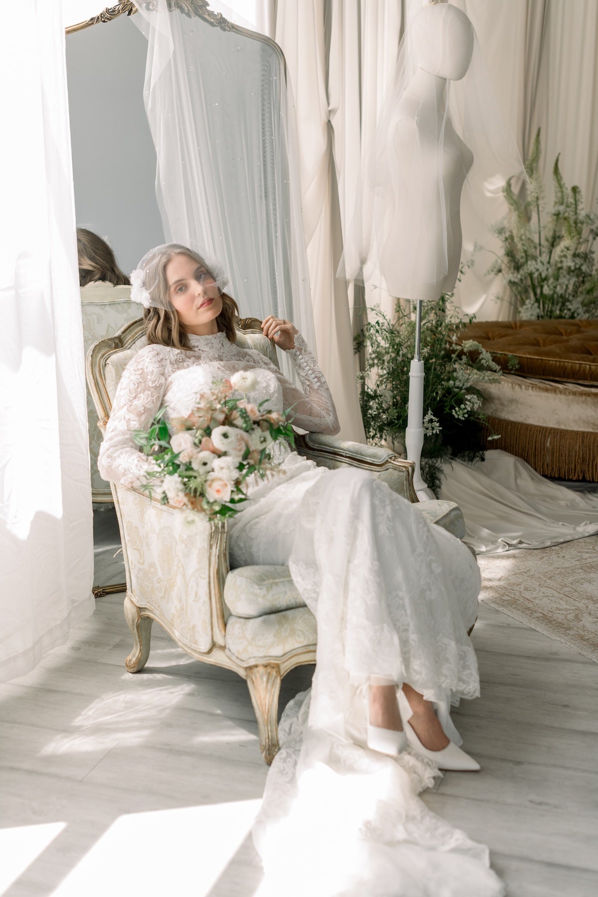 Woman in a white dress holding flowers in a room with a mirror and mannequin.