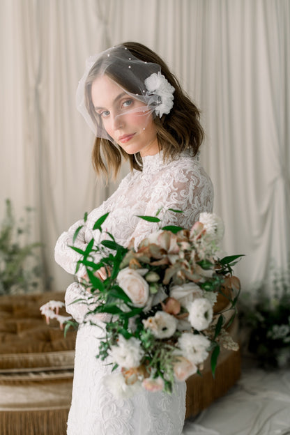 Woman in a white lace dress holding a bouquet of flowers with a veil and floral headband.
