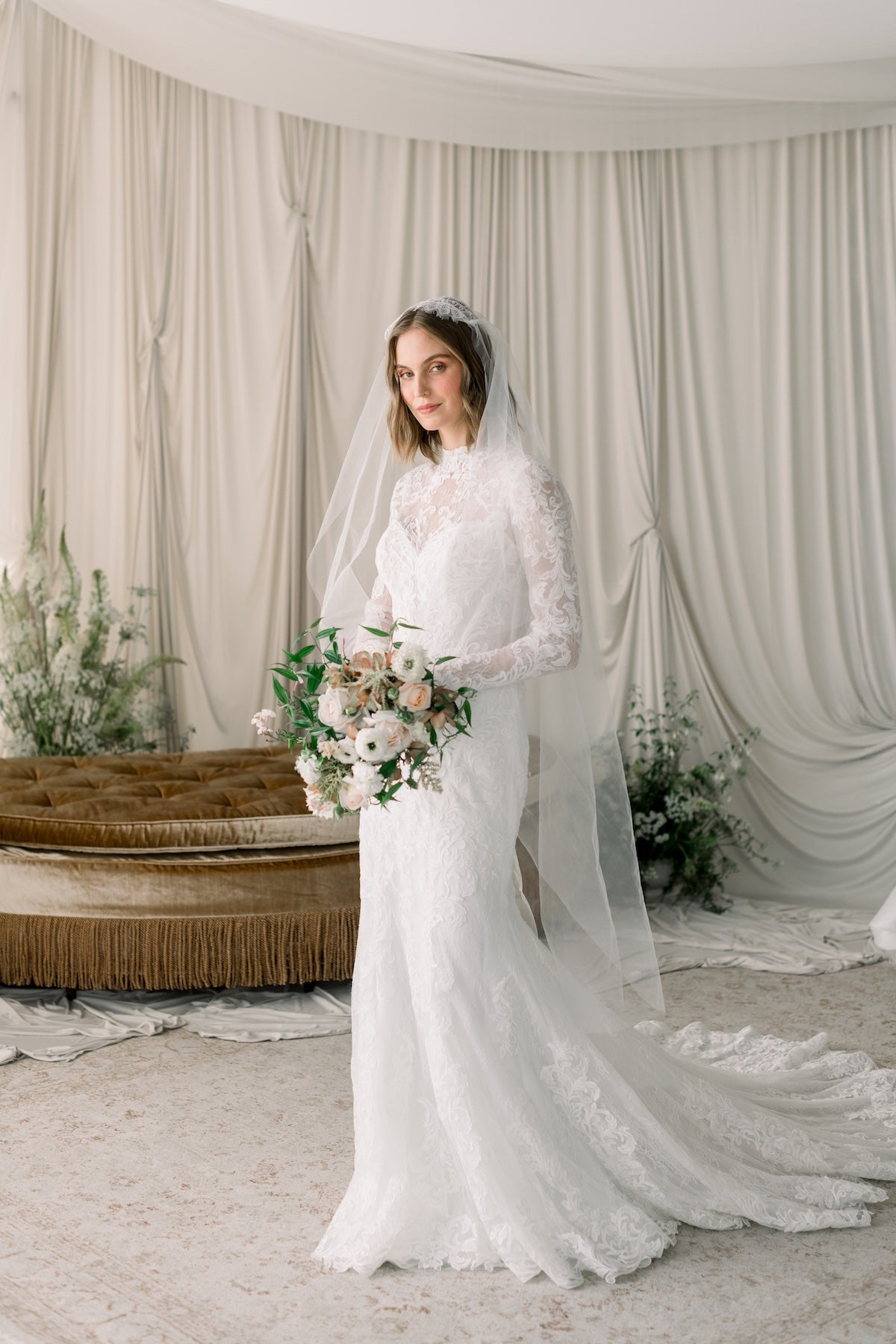 Bride in a white wedding dress with a long veil standing in a decorated room.