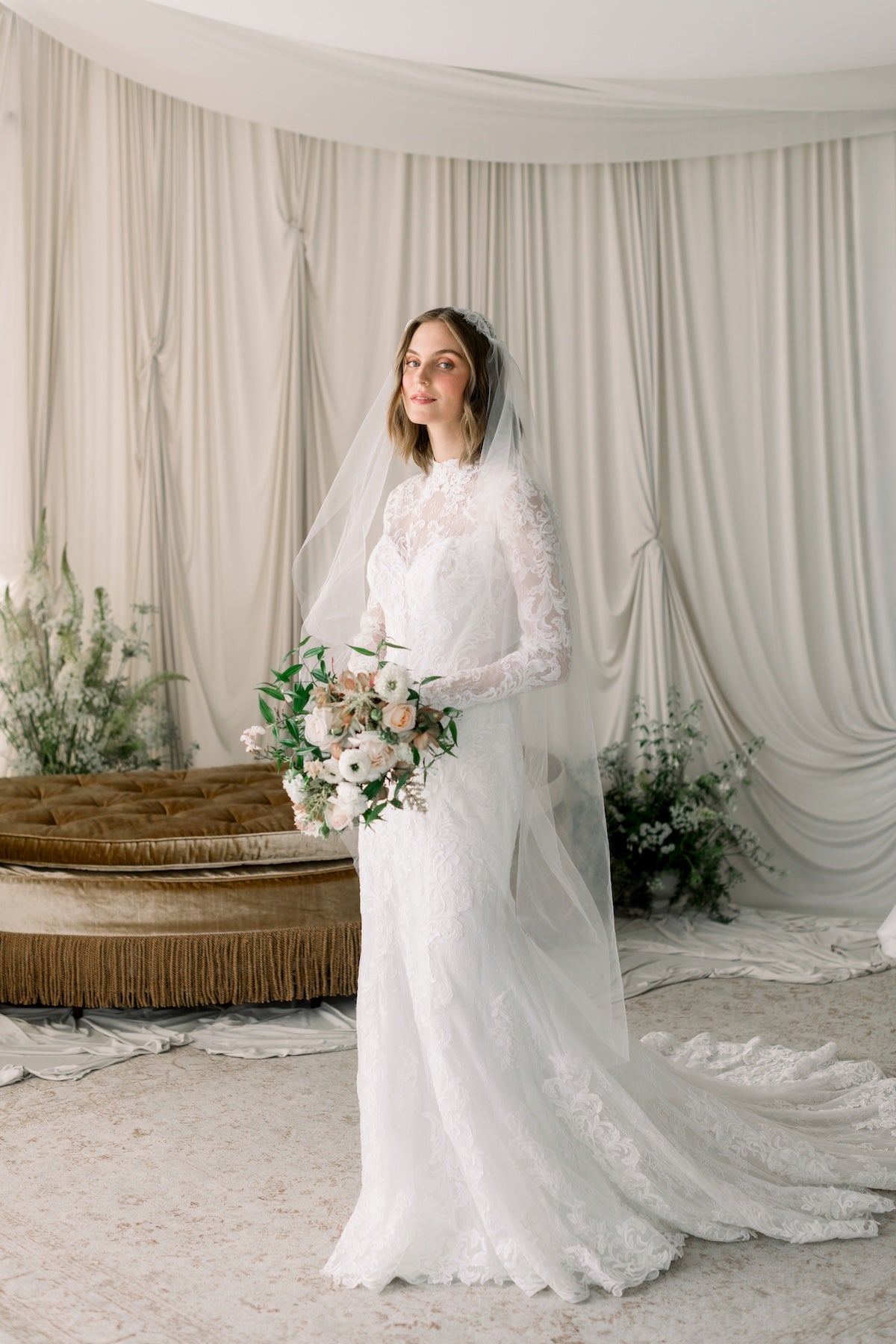 Woman in a white wedding dress standing in a decorated room with floral arrangements.