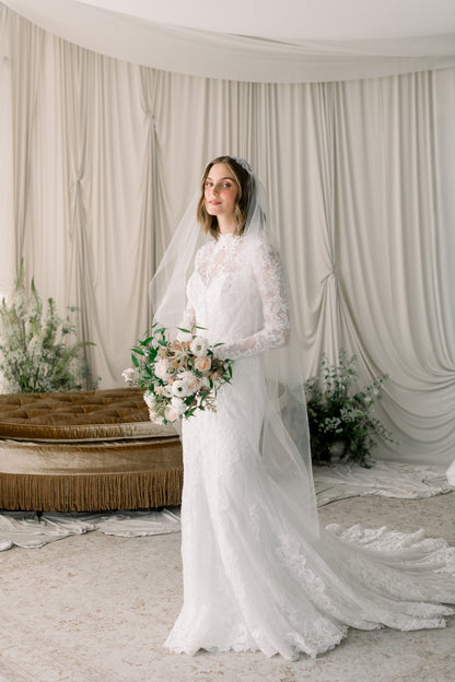 Woman in a white wedding dress standing in a decorated room with floral arrangements.