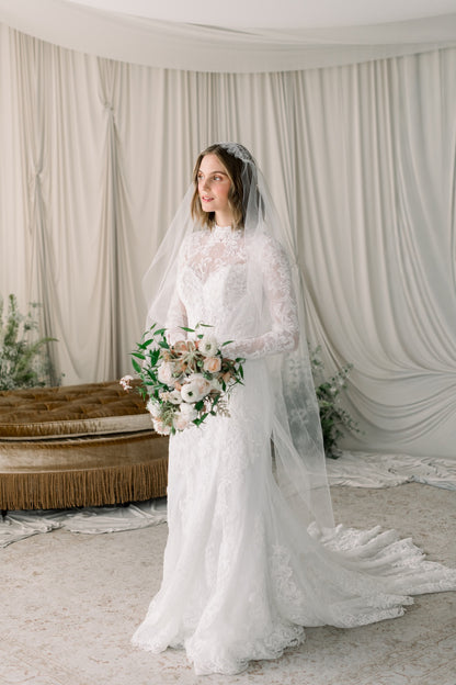 Woman in a white wedding dress with a veil holding a bouquet in a decorated room.