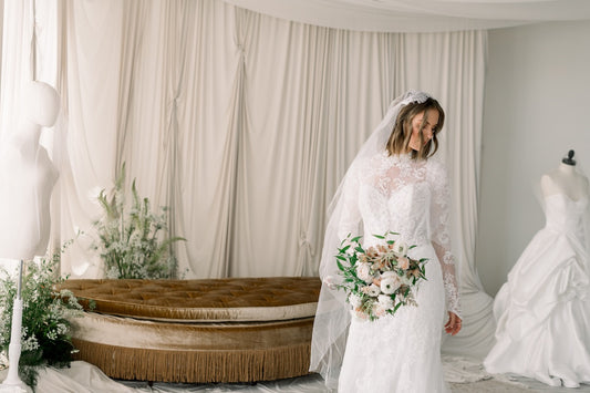 Woman in a wedding dress holding a bouquet in a bridal shop with mannequins and decor.
