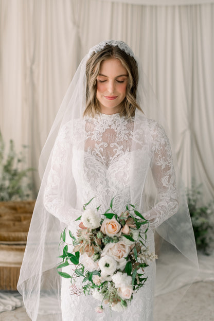 Bride in a white lace wedding dress holding a bouquet with a neutral background