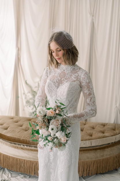 Woman in a lace wedding dress holding a bouquet in a softly lit room.