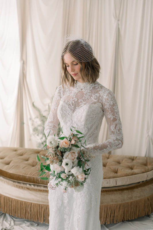 Woman in a lace wedding dress holding a bouquet in a softly lit room.