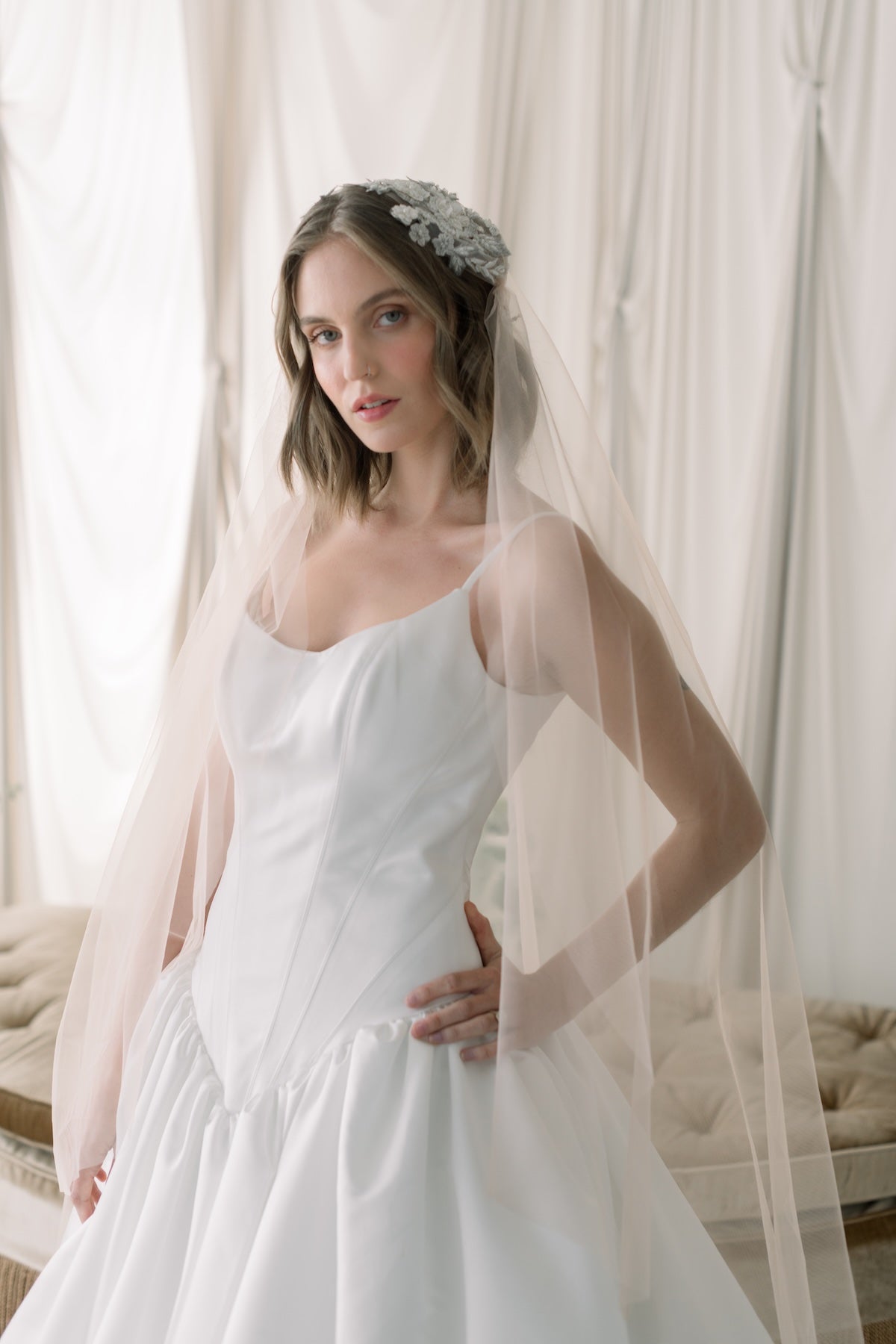 Woman in a white wedding dress with a veil standing in front of light curtains.