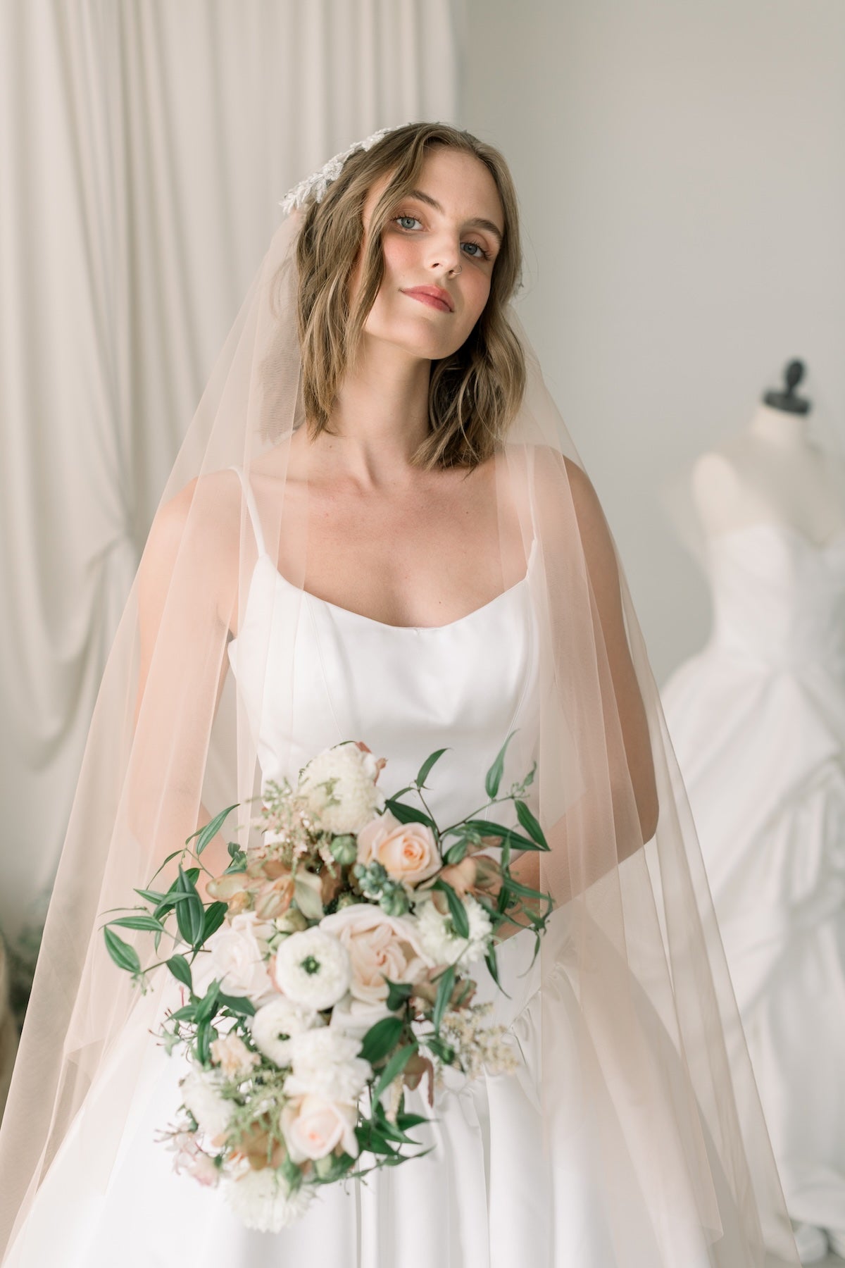 Bride holding a bouquet with a wedding dress in the background