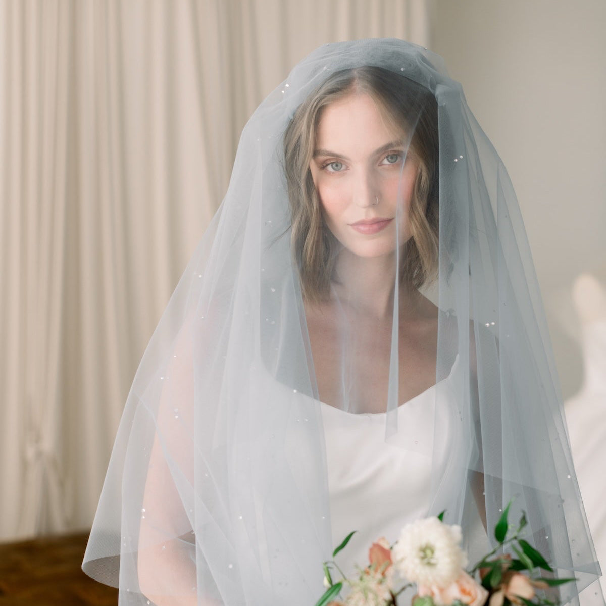 Bride wearing a light blue veil holding a bouquet indoors.