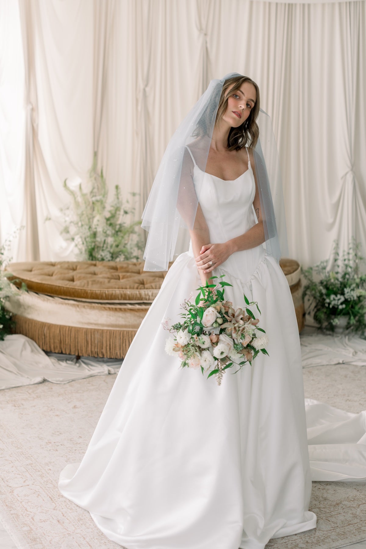 Bride in a white wedding dress holding a bouquet in a decorated room.