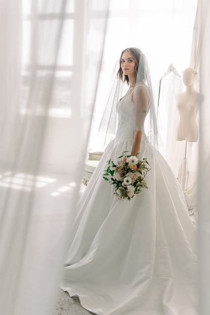 Woman in a white wedding dress holding a bouquet of flowers in a softly lit room.