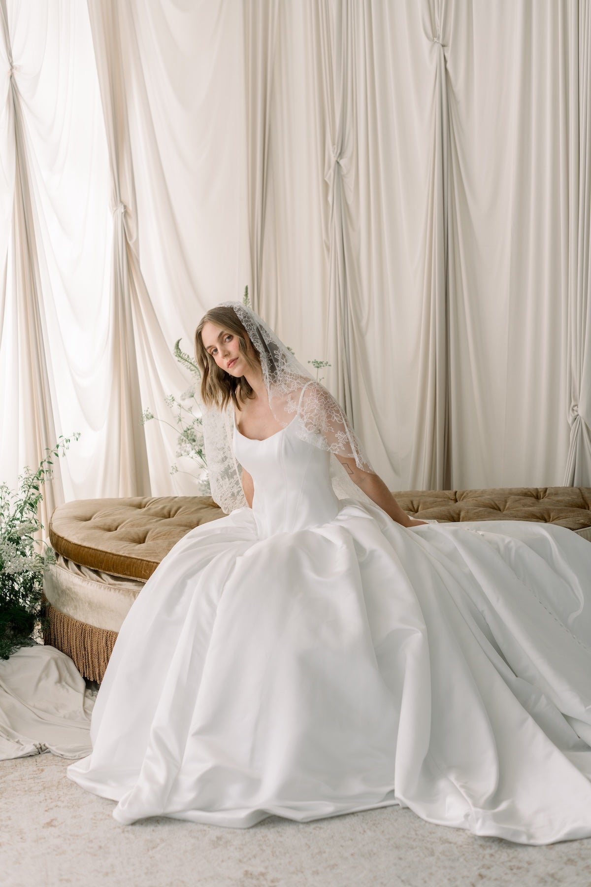 Woman in a white wedding dress sitting on a couch with a neutral background