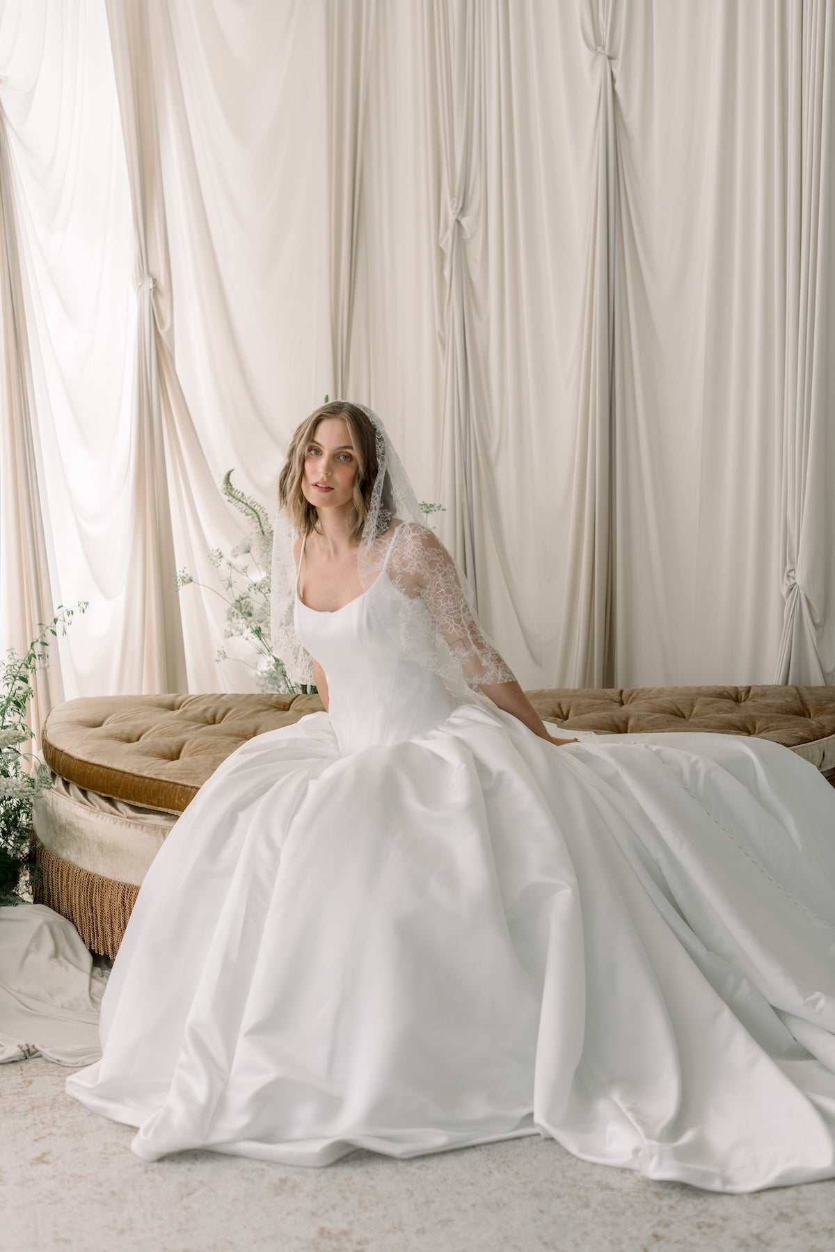 Woman in a white wedding dress sitting on a couch with a neutral background