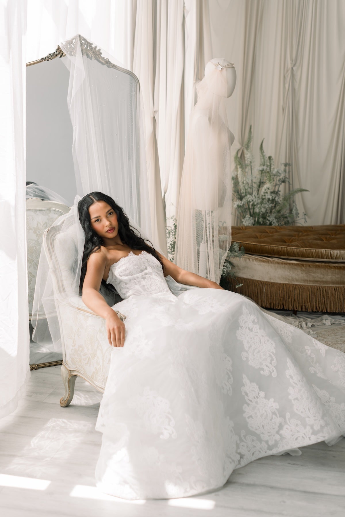 Woman in a white wedding dress sitting in a room with white curtains and decor.