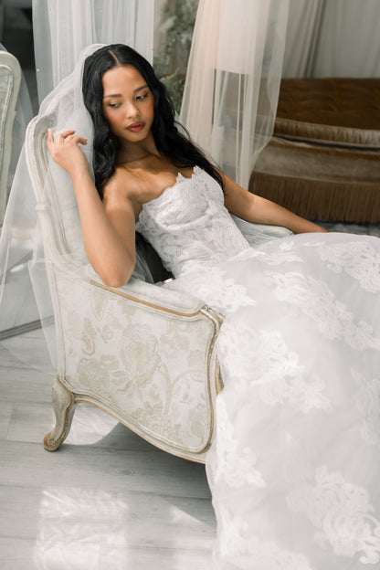 Woman in a white wedding dress sitting on a decorative chair.