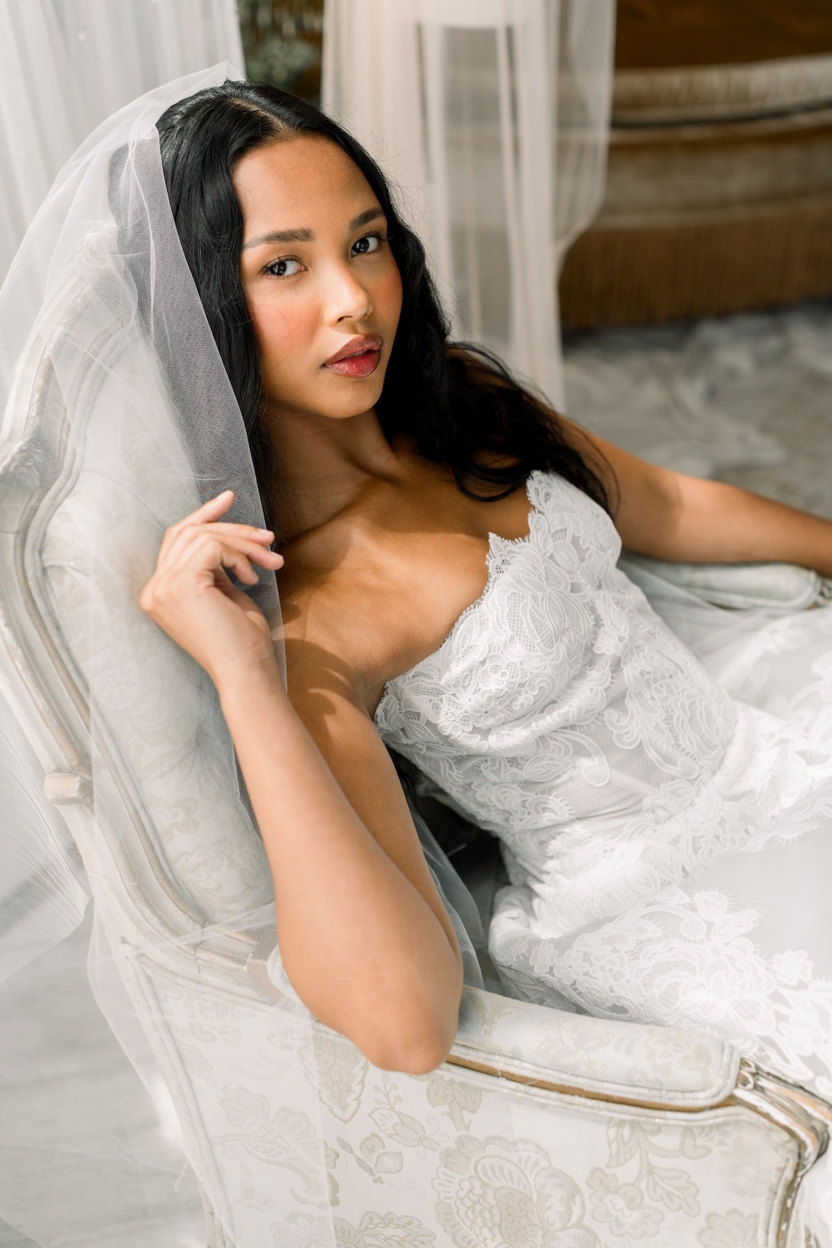 Woman in a white lace dress sitting in a decorative chair with a veil.
