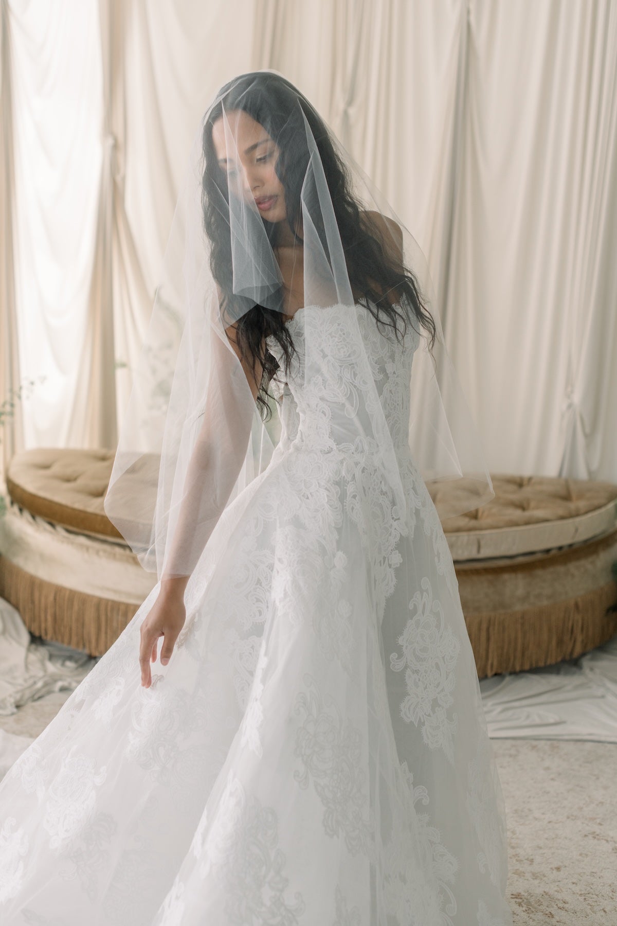 Woman in a white wedding dress with a veil standing in front of a curtain.