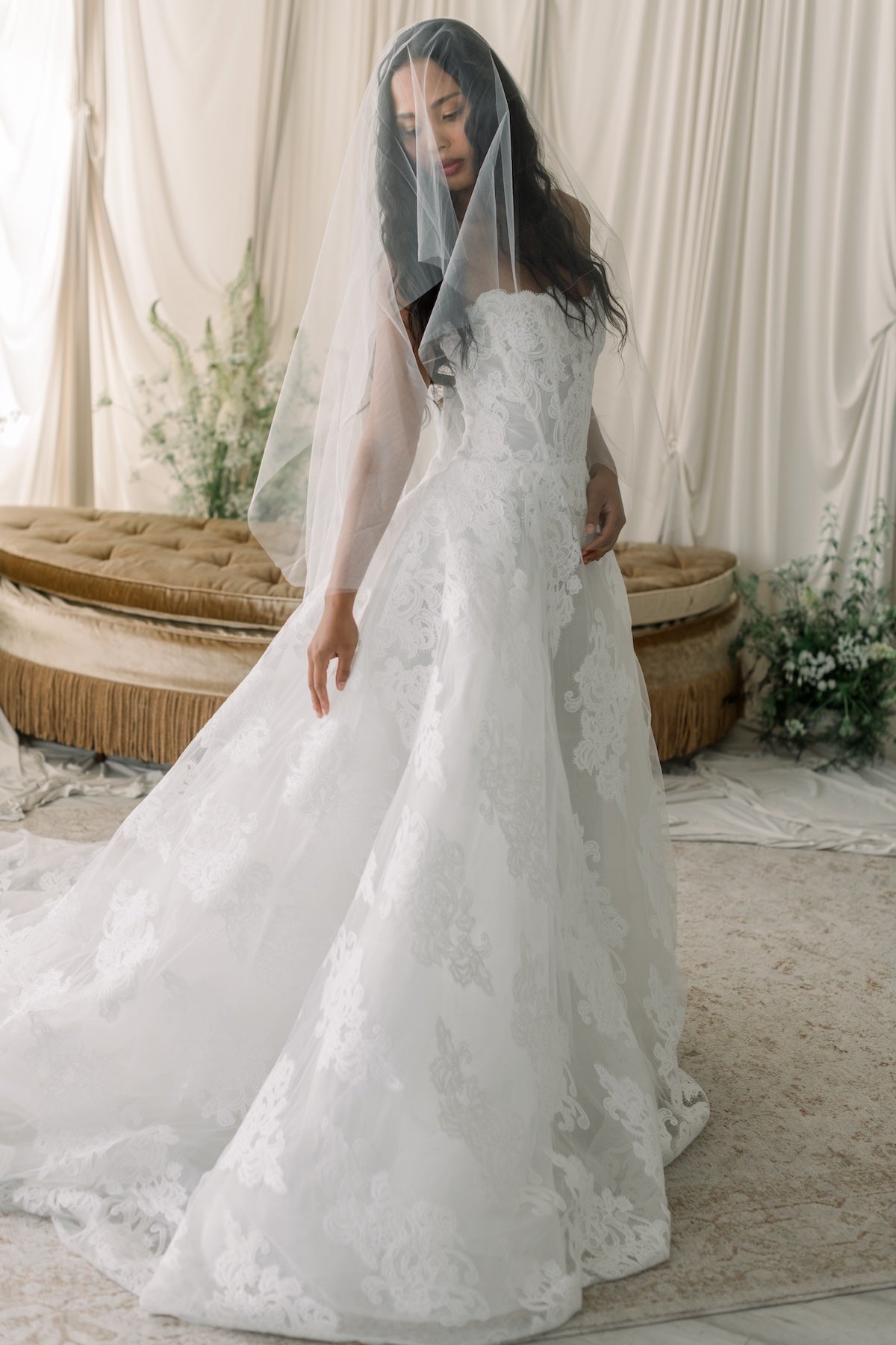 Woman in a white lace wedding dress with a veil in a softly lit room.